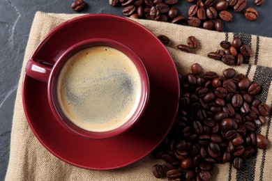 Photo of Cup of hot aromatic coffee and roasted beans on black table, flat lay