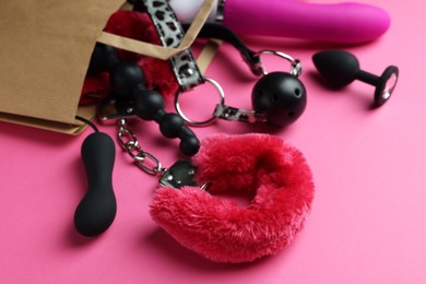 Photo of Paper shopping bag with different sex toys on pink background, closeup