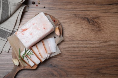 Pork fatback with rosemary, garlic and peppercorns on wooden table, flat lay. Space for text