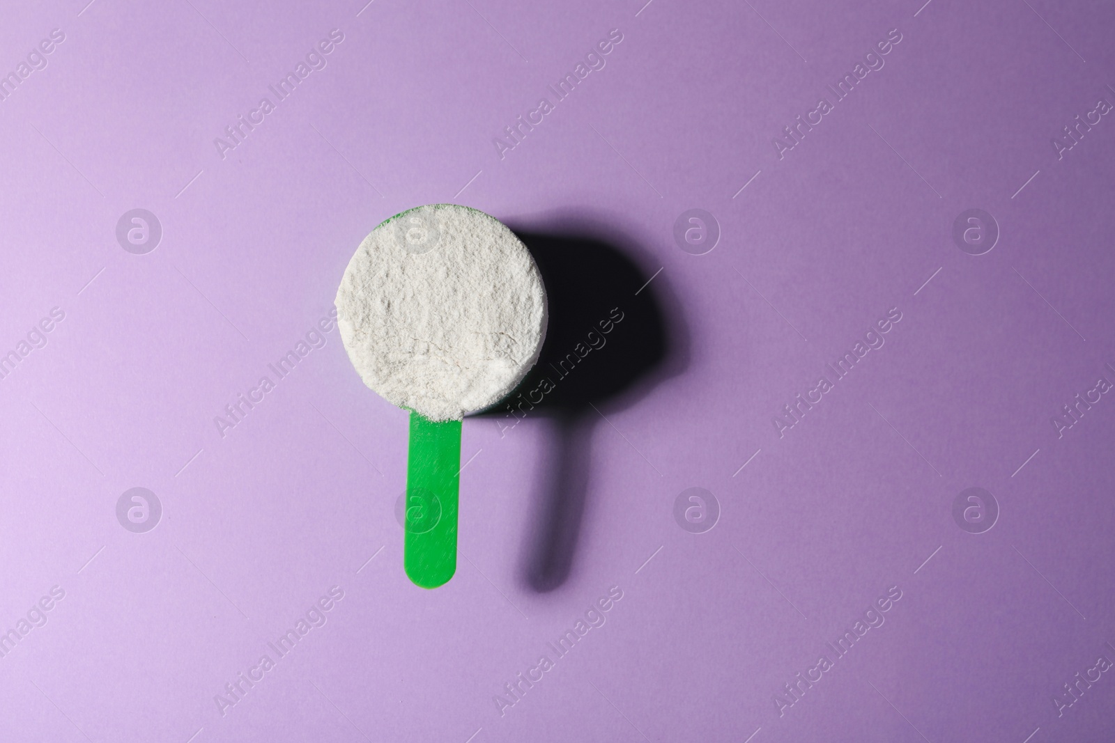 Photo of Scoop of protein powder on violet background, top view with space for text