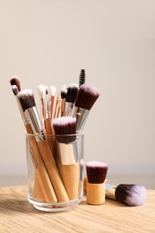 Set of professional makeup brushes on wooden table against beige background