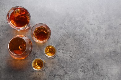 Different delicious liqueurs in glasses on grey table, flat lay. Space for text