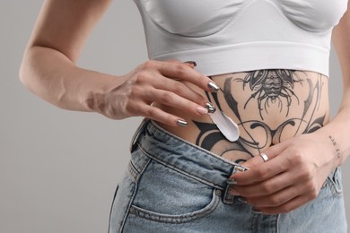 Photo of Woman applying healing cream onto her tattoos against grey background, closeup