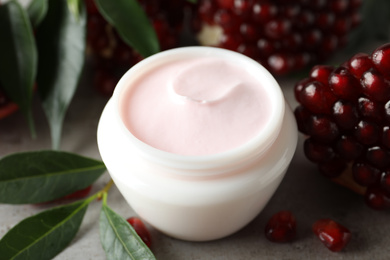 Natural facial mask, pomegranate seeds and green leaves on light grey table, closeup