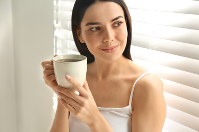 Photo of Young woman with cup of tea near window. Lazy morning