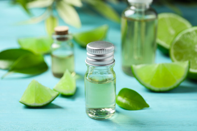 Photo of Lime essential oil and cut citrus fruits on light blue wooden table