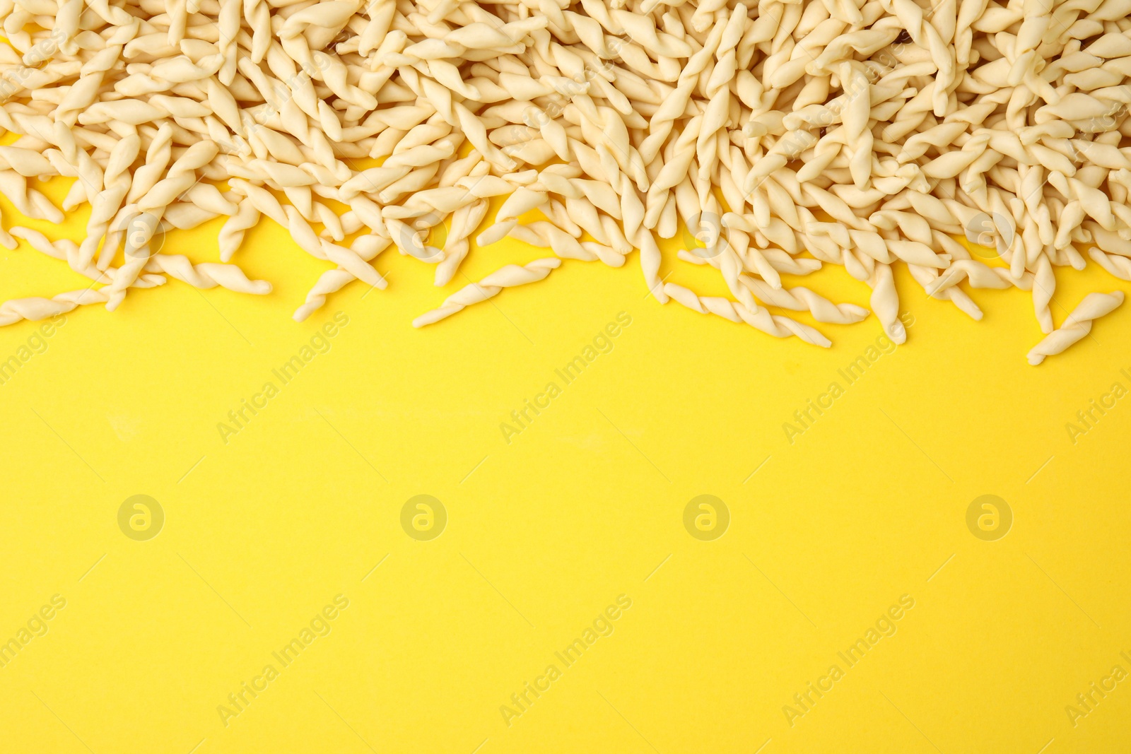 Photo of Uncooked trofie pasta on yellow background, flat lay. Space for text