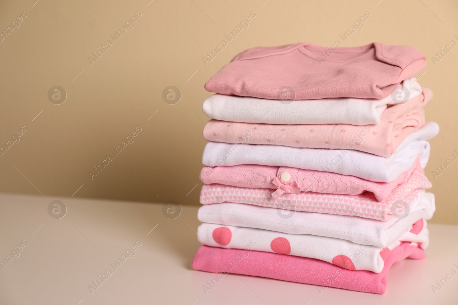 Photo of Stack of baby girl's clothes on white table. Space for text