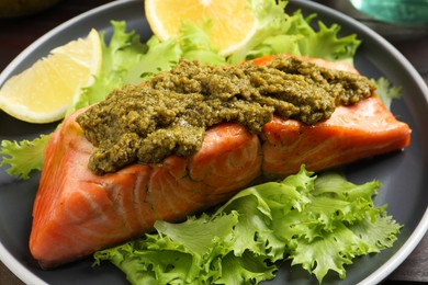 Photo of Delicious cooked salmon with pesto sauce, lettuce and lemon on plate, closeup