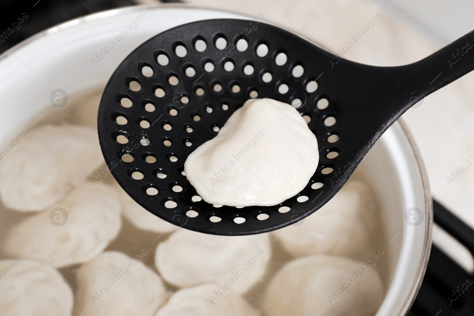 Photo of Dumpling (varenyk) with tasty filling on skimmer over pot, closeup
