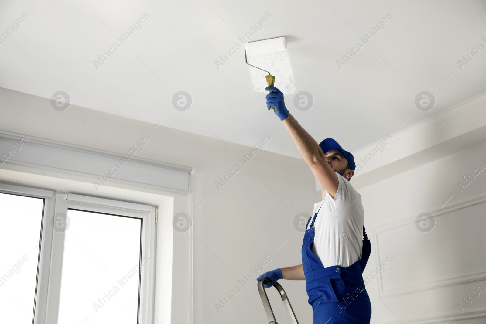 Photo of Handyman painting ceiling with white dye indoors, space for text