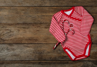 Cute striped baby bodysuit and candy canes on wooden background, flat lay with space for text. Christmas outfit