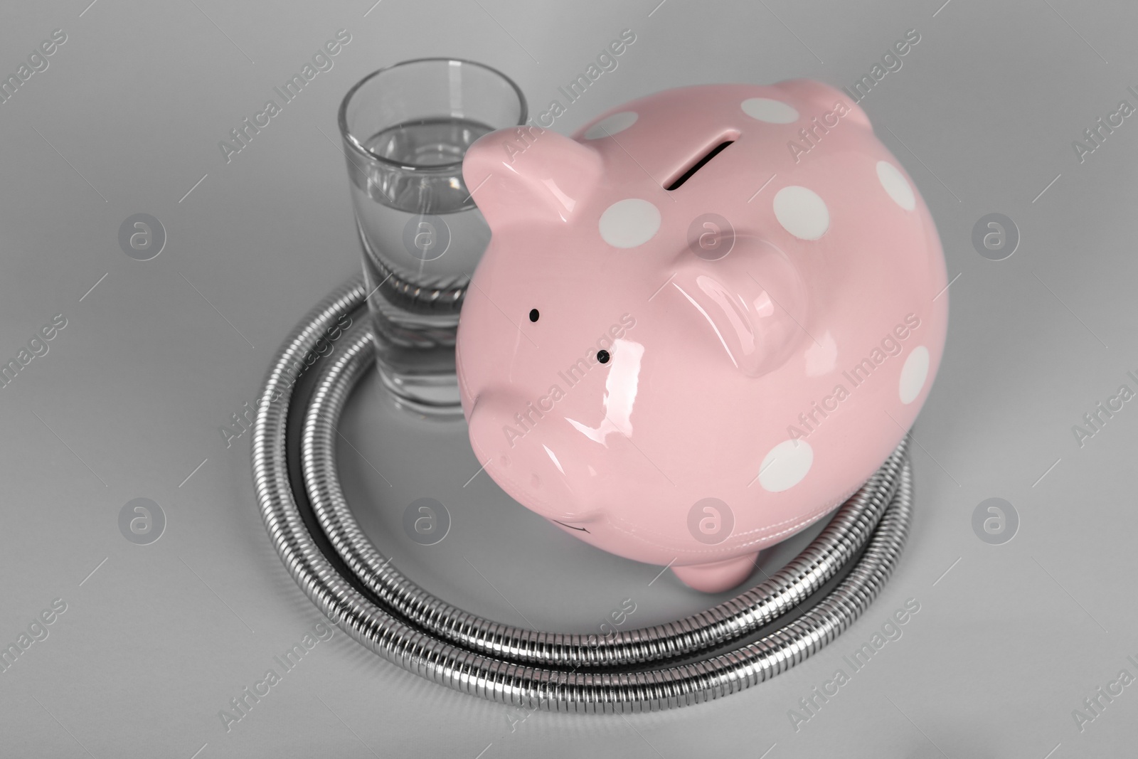 Photo of Water scarcity concept. Piggy bank, shower hose and glass of drink on grey background