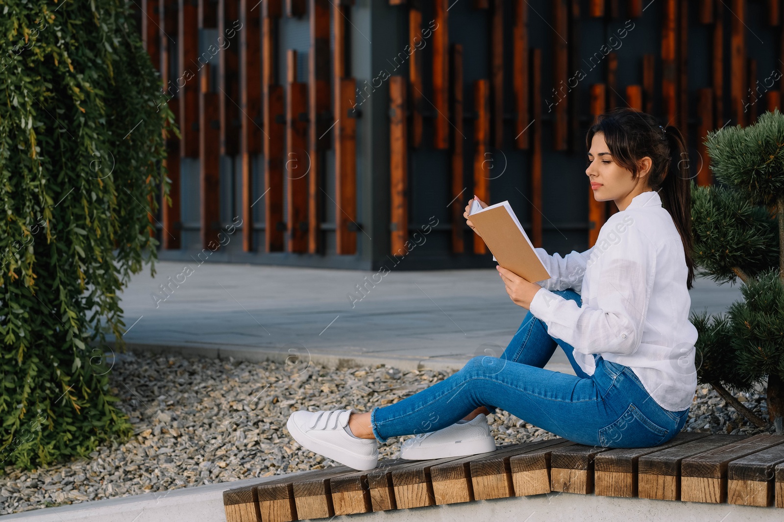 Photo of Young woman reading book on bench outdoors