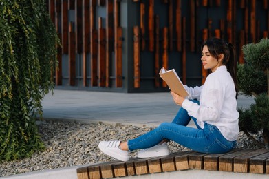 Young woman reading book on bench outdoors
