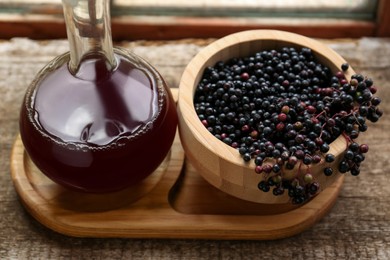 Photo of Elderberry wine and bowl with Sambucus berries on wooden table