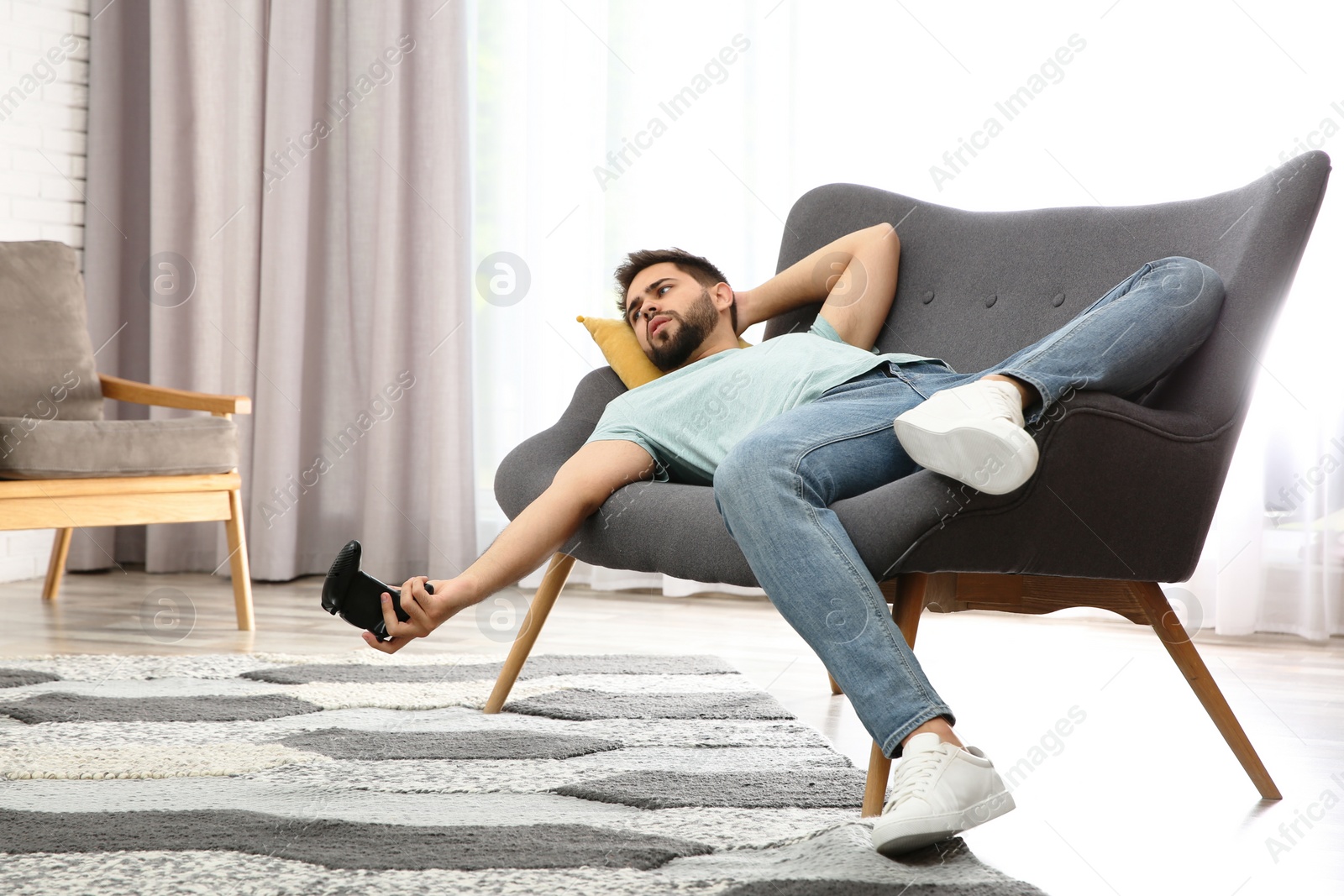 Photo of Lazy young man playing video game while lying on sofa at home