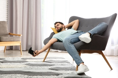 Lazy young man playing video game while lying on sofa at home