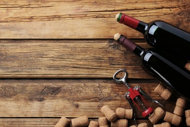 Bottles with wine, corkscrew and corks on wooden table, flat lay. Space for text
