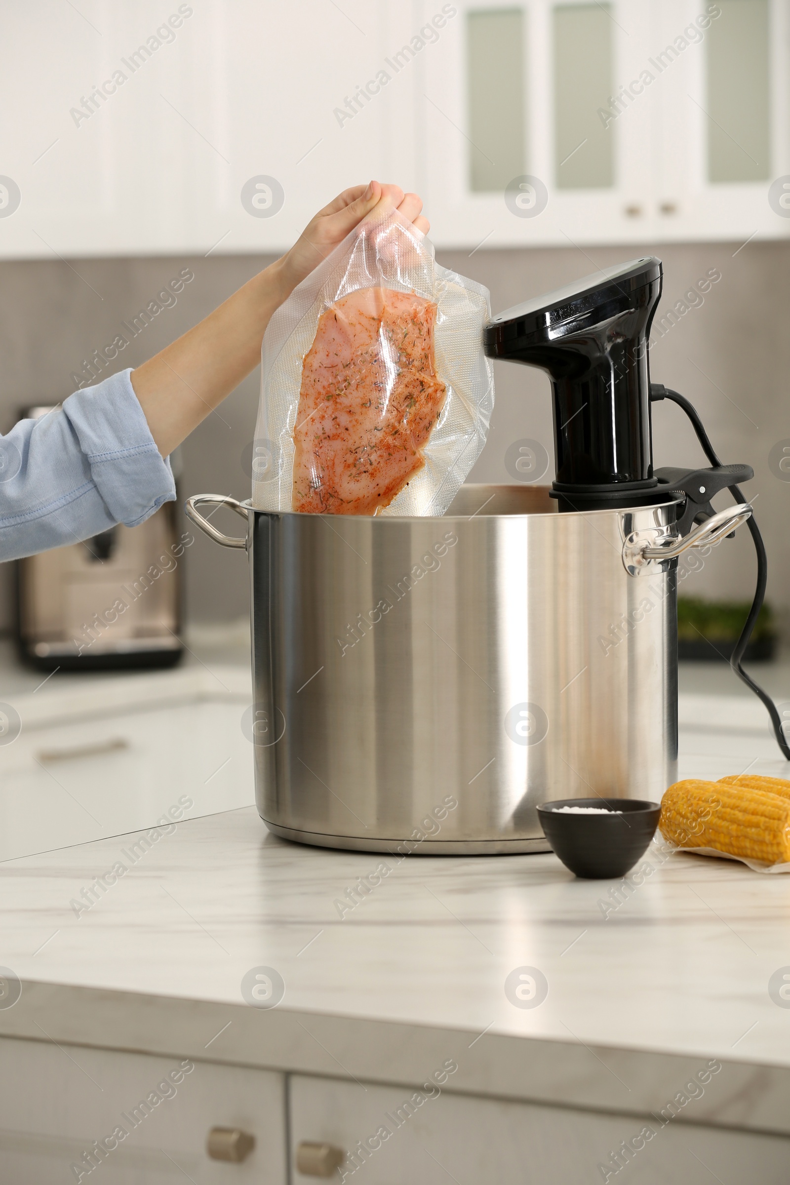 Photo of Woman putting vacuum packed meat into pot with sous vide cooker in kitchen, closeup. Thermal immersion circulator