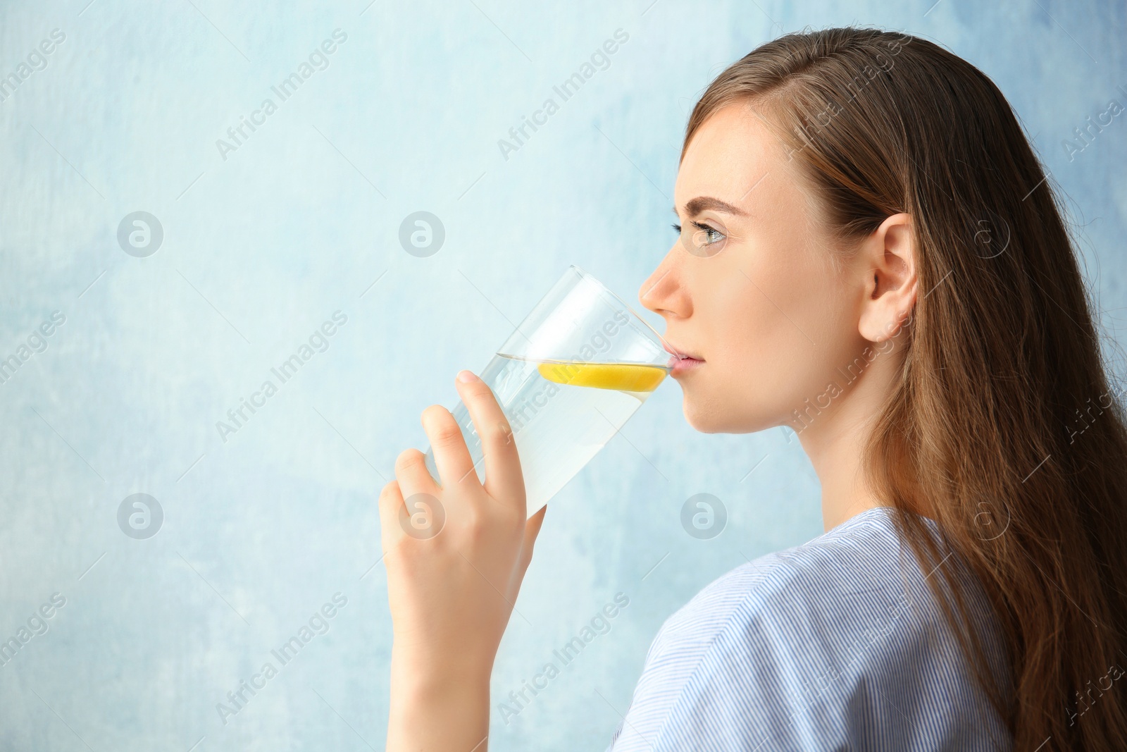 Photo of Young woman drinking water with lemon against color background