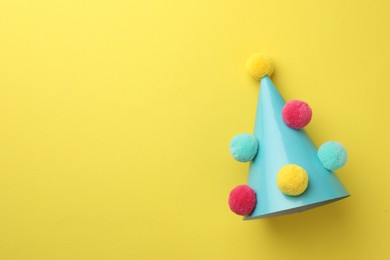 Photo of One light blue party hat with pompoms on yellow background, top view