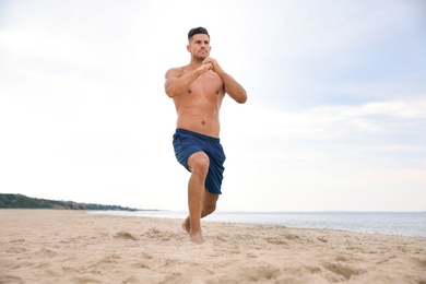 Photo of Muscular man doing exercise on beach. Body training