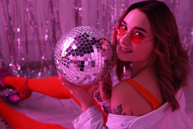 Beautiful woman in stylish outfit with disco ball at party indoors, toned in pink