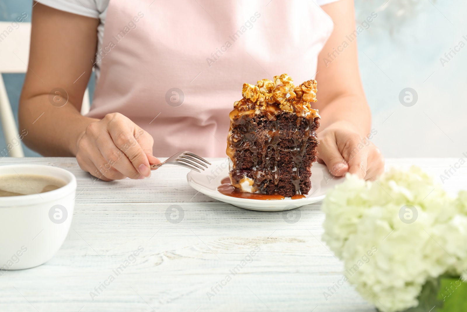 Photo of Woman eating delicious homemade cake with caramel sauce and popcorn at table