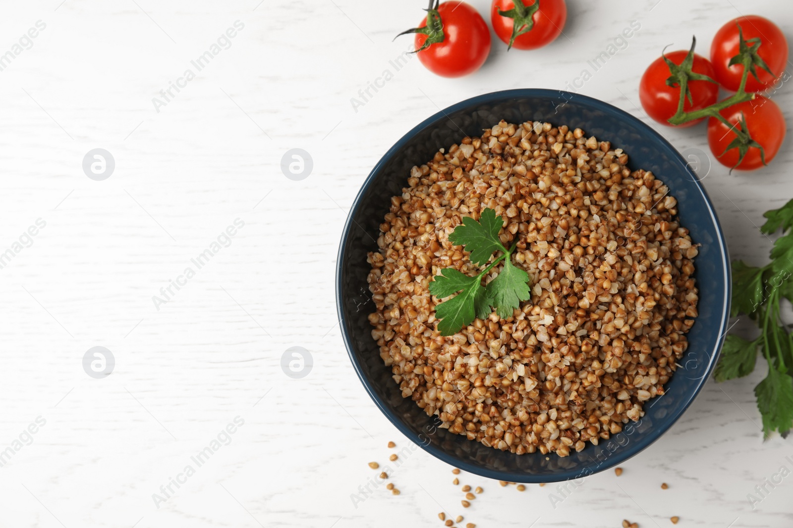 Photo of Bowl of buckwheat porridge with tomatoes and parsley on white table, flat lay. Space for text