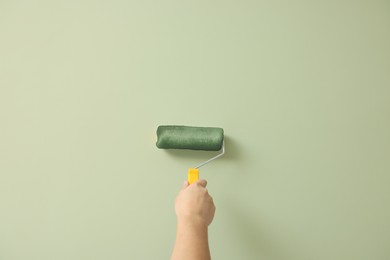 Worker using roller to paint wall with pale olive dye, closeup