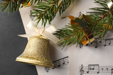 Photo of Golden shiny bell with white bow, fir branches and music sheets on grey table, top view. Christmas decoration