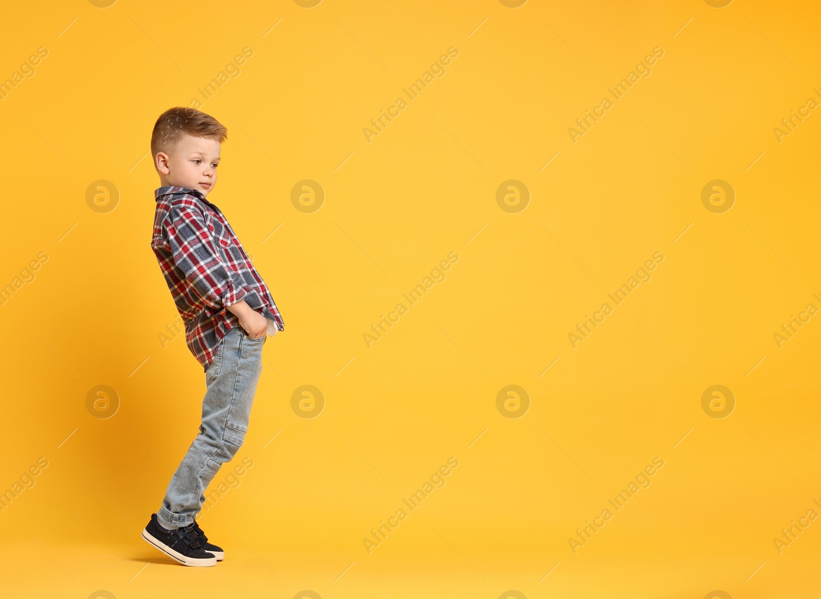 Photo of Happy little boy dancing on yellow background. Space for text