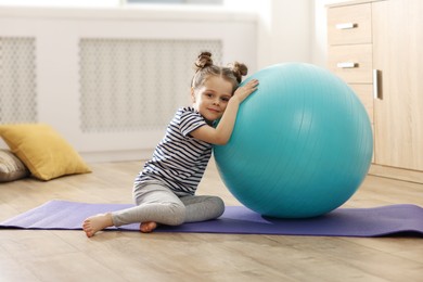 Little cute girl with fitness ball at home. Doing exercises