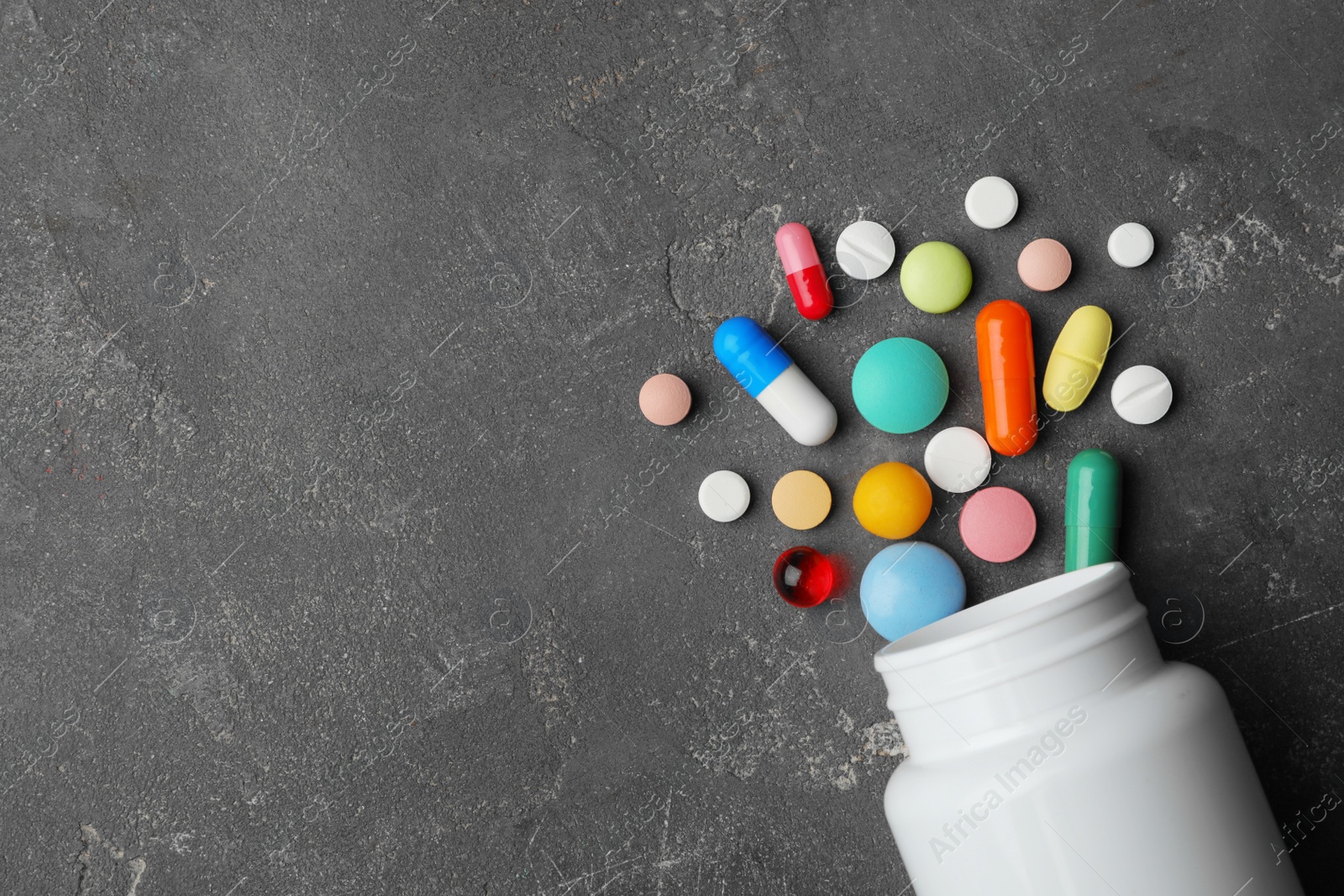 Photo of Bottle with different pills on grey background, flat lay. Space for text