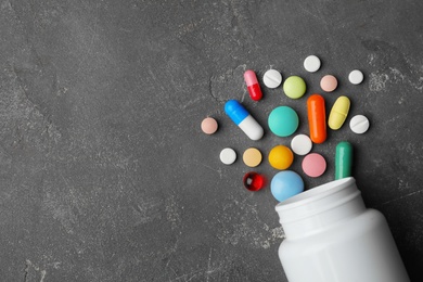 Bottle with different pills on grey background, flat lay. Space for text