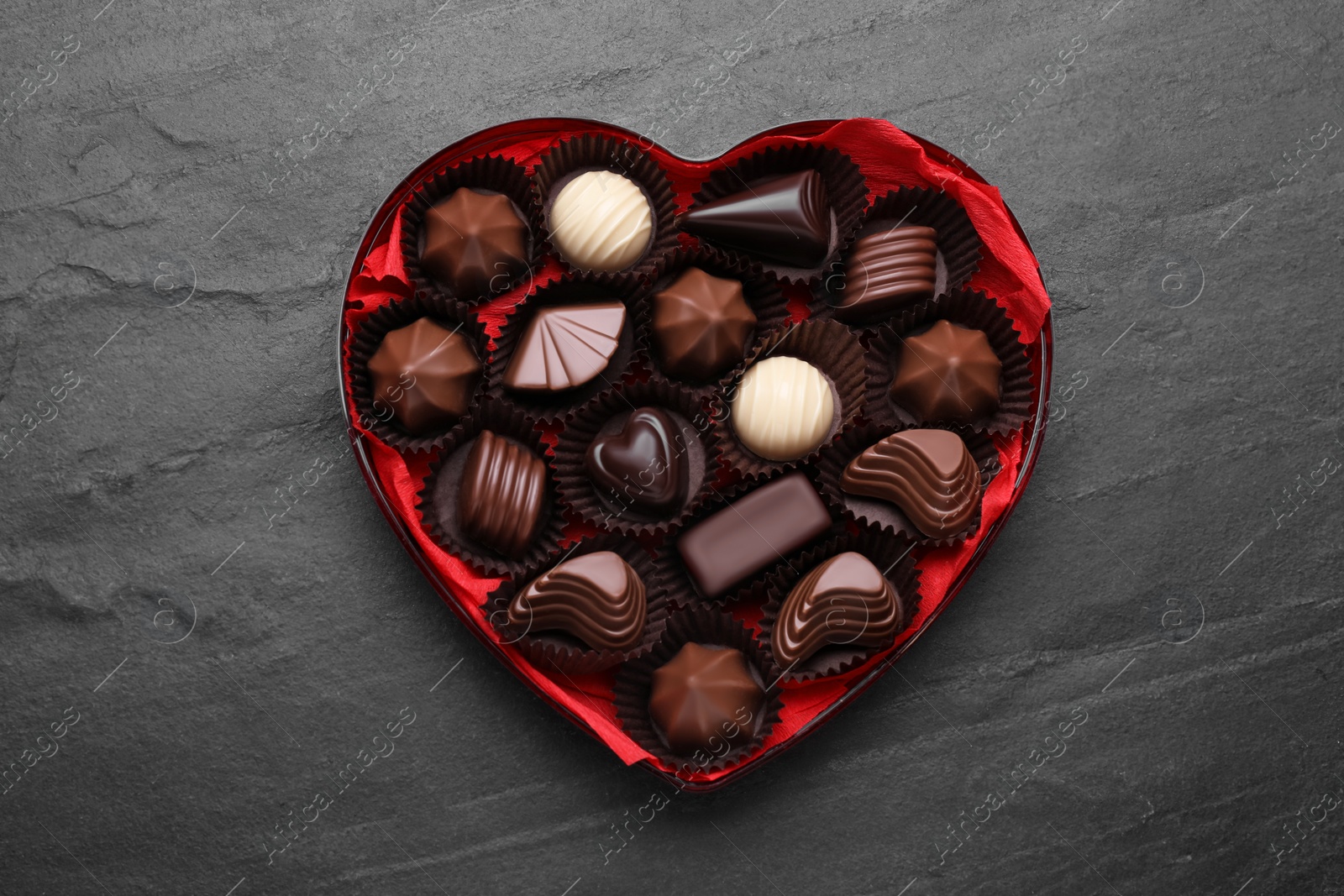 Photo of Heart shaped box with delicious chocolate candies on black table, top view