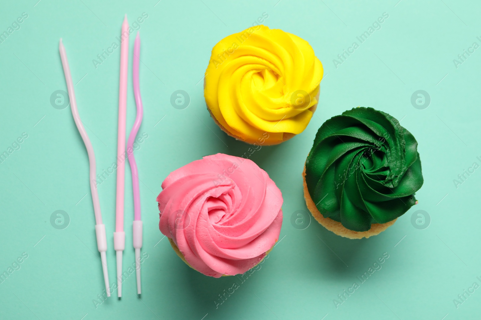 Photo of Delicious cupcakes with bright cream and candles on turquoise background, flat lay