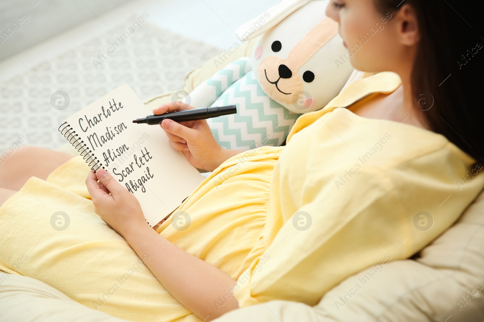 Photo of Pregnant woman with baby names list sitting in armchair, closeup