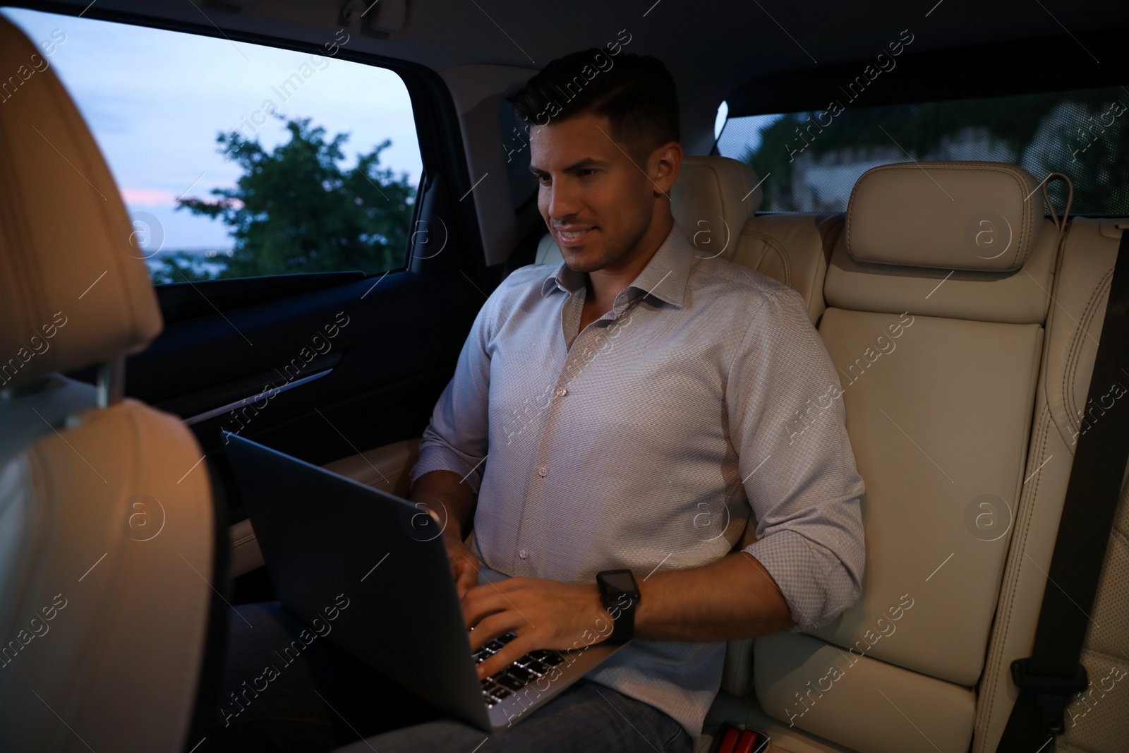 Photo of Handsome man working with laptop on backseat of modern car