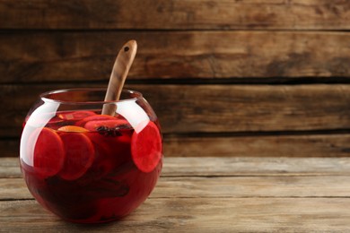 Photo of Glass bowl of delicious aromatic punch drink and ladle on wooden table. Space for text