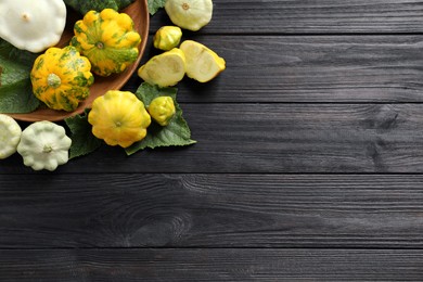 Fresh ripe pattypan squashes with leaves on black wooden table, flat lay. Space for text