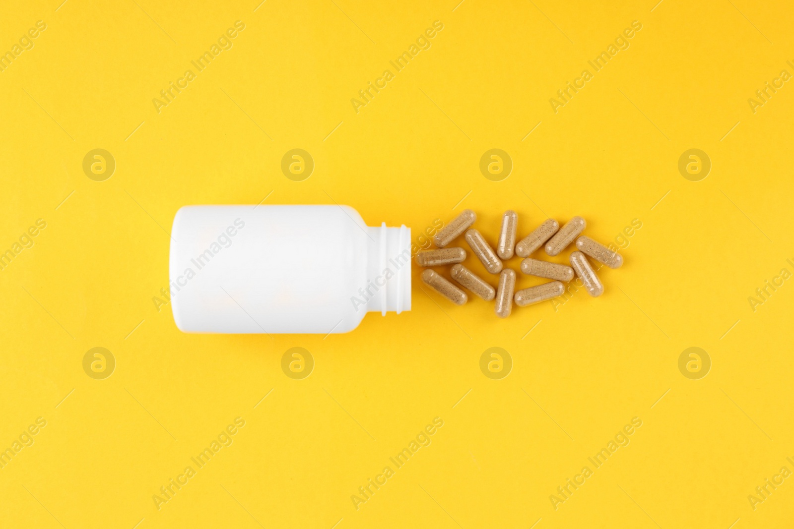 Photo of White medical bottle and vitamin capsules on yellow background, top view