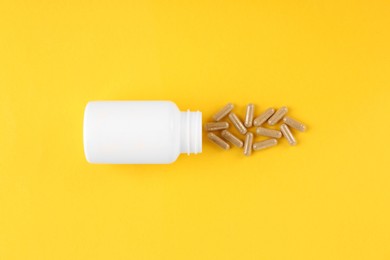 White medical bottle and vitamin capsules on yellow background, top view