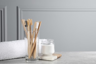 Bamboo toothbrushes, towel and jar of baking soda on light grey table, space for text