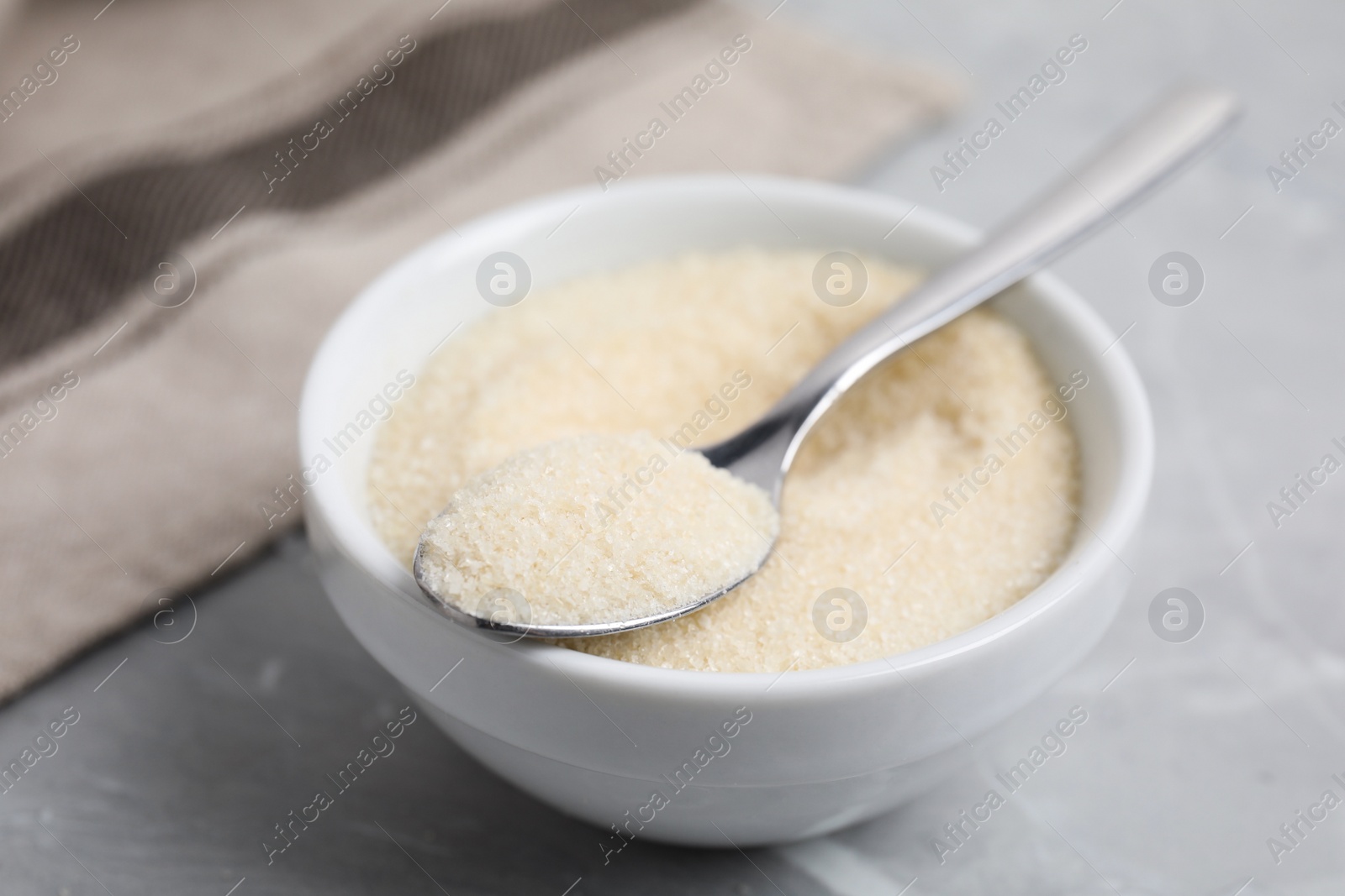 Photo of Gelatin powder in bowl and spoon on light grey marble table, closeup