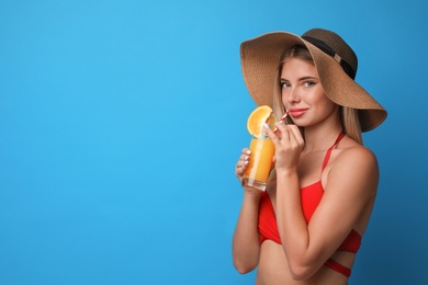 Pretty young woman wearing stylish bikini with cocktail on blue background. Space for text