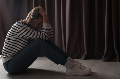 Sad young woman sitting on floor indoors, space for text