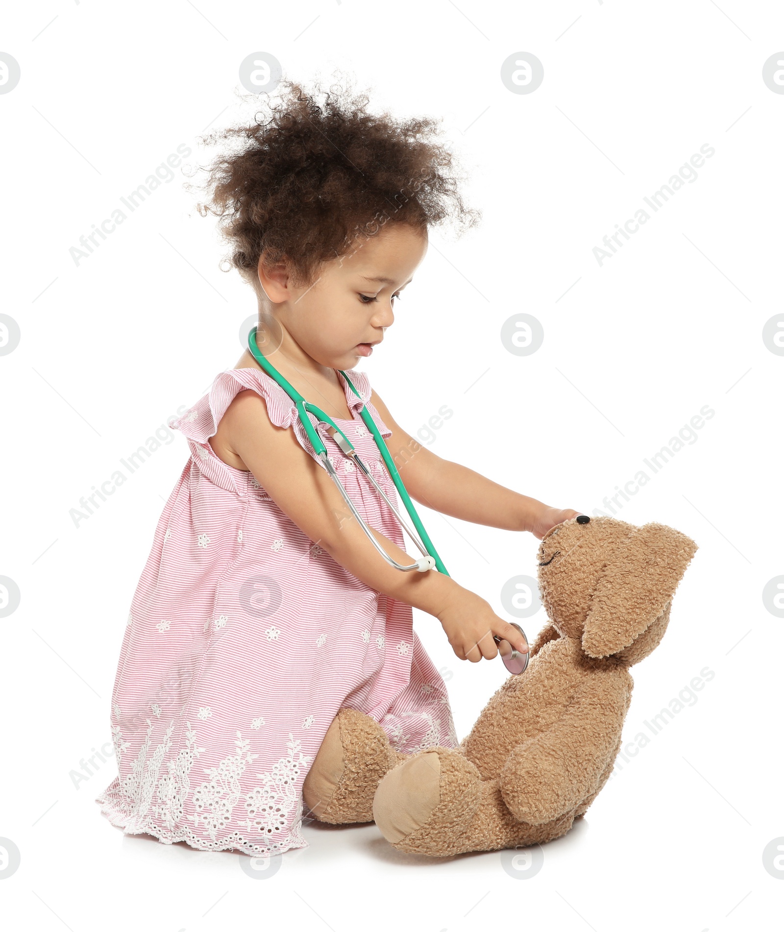 Photo of Cute African American child imagining herself as doctor while playing with stethoscope and toy bunny on white background