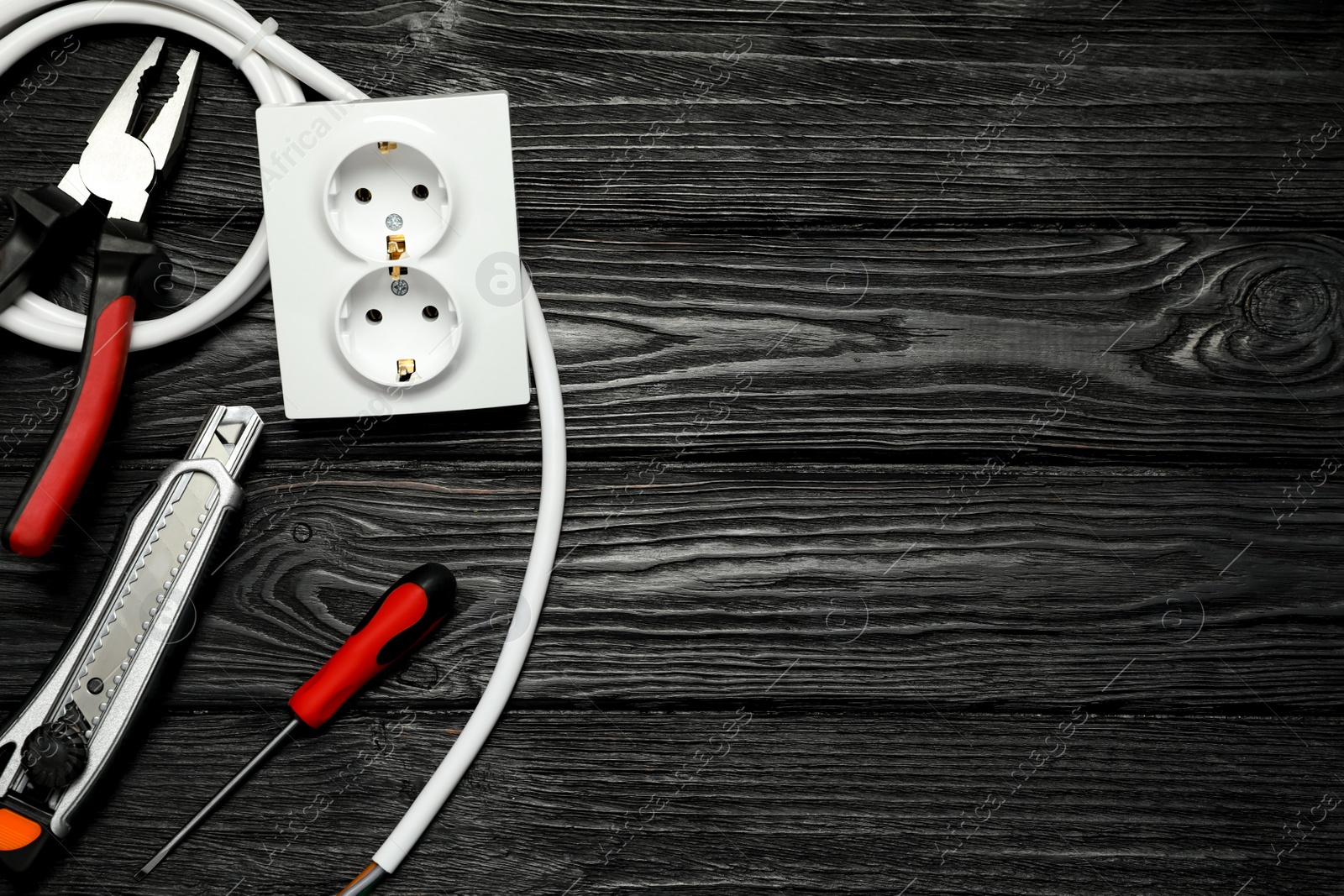 Photo of Set of electrician's tools and power socket on black wooden table, flat lay. Space for text